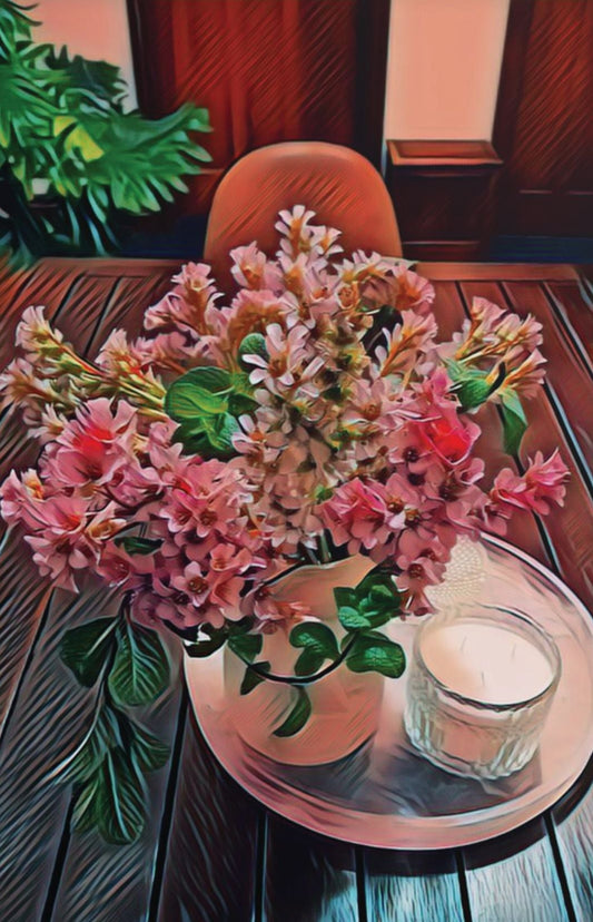 A poster print of a still life composition with a vase of pink and red flowers on a table, with a candle and a glass in the foreground. The print has a warm, matte finish.