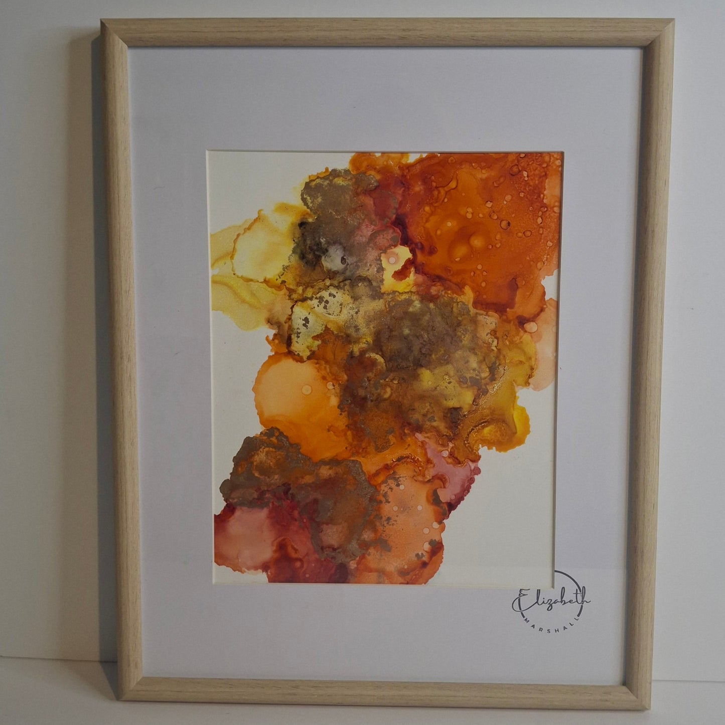 Framed abstract alcohol ink painting in warm golden amber and earthy rust tones titled Into the Light by Elizabeth Marshall.