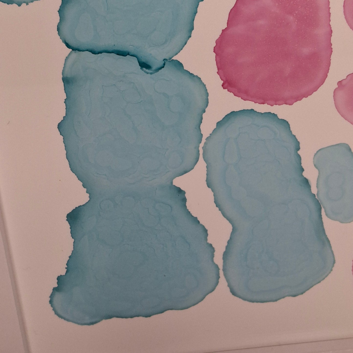 Framed abstract alcohol ink painting titled Currents of Love by Elizabeth Marshall, featuring organic flowing shapes in soft blue and vibrant pink, evoking coral reefs and ocean currents.