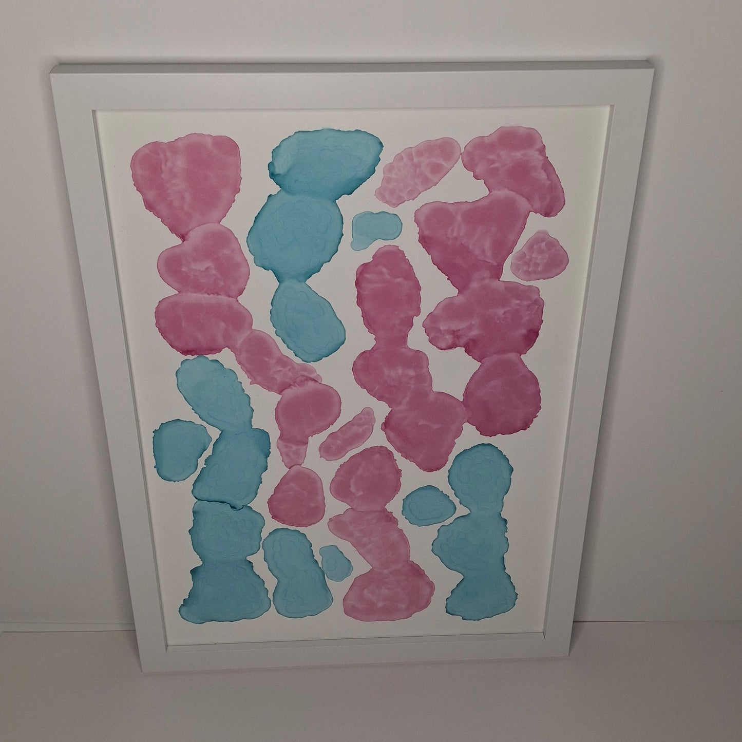 Framed artwork with pink and blue abstract shapes on a white background