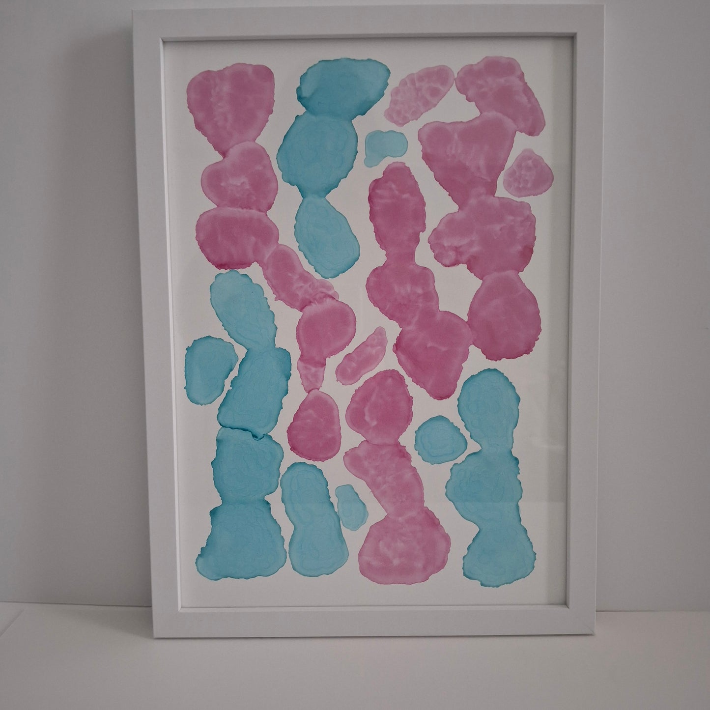 Framed abstract artwork with pink and blue shapes on a white background