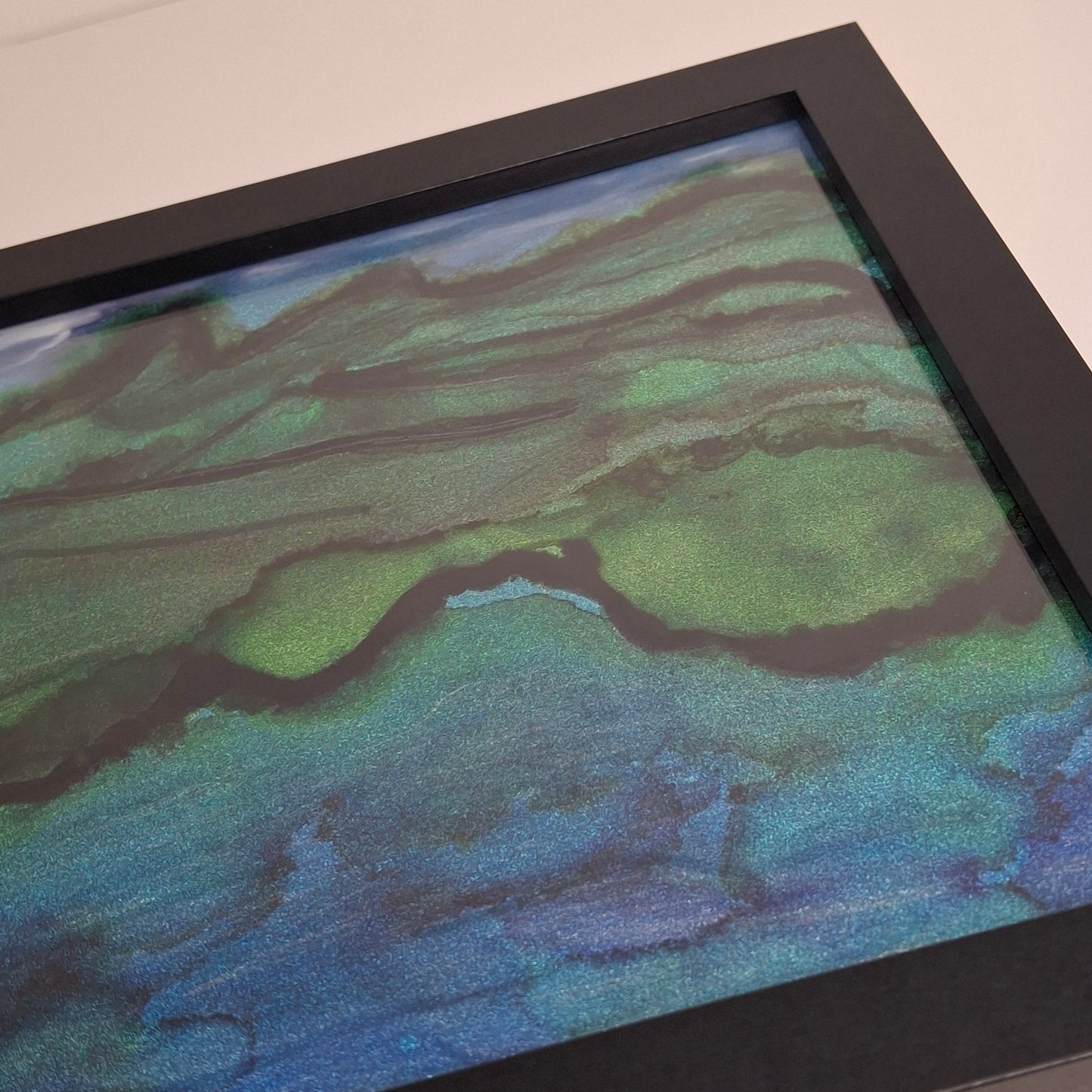 Close-up of a framed abstract artwork with green and blue hues.