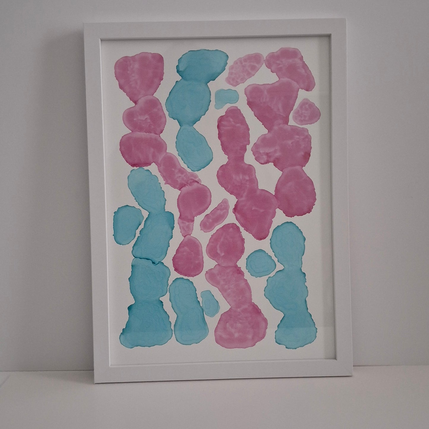 Framed abstract artwork with pink and blue shapes on a white wall