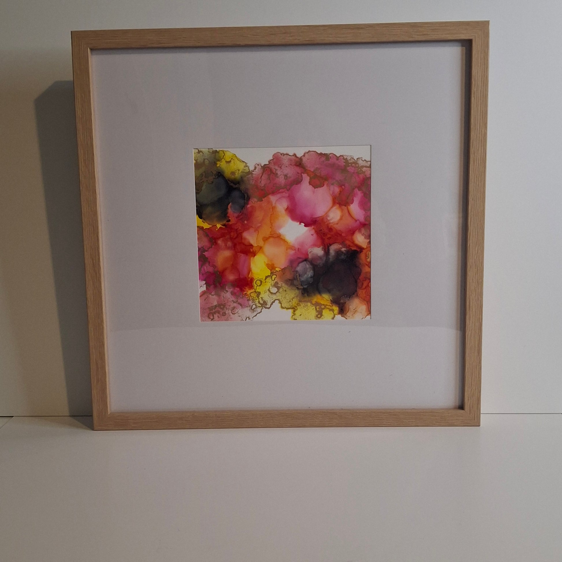 Framed original alcohol ink artwork featuring flowing pink, orange, yellow and charcoal tones in a square composition, titled "Between the Veils" from the Invisible Currents collection.