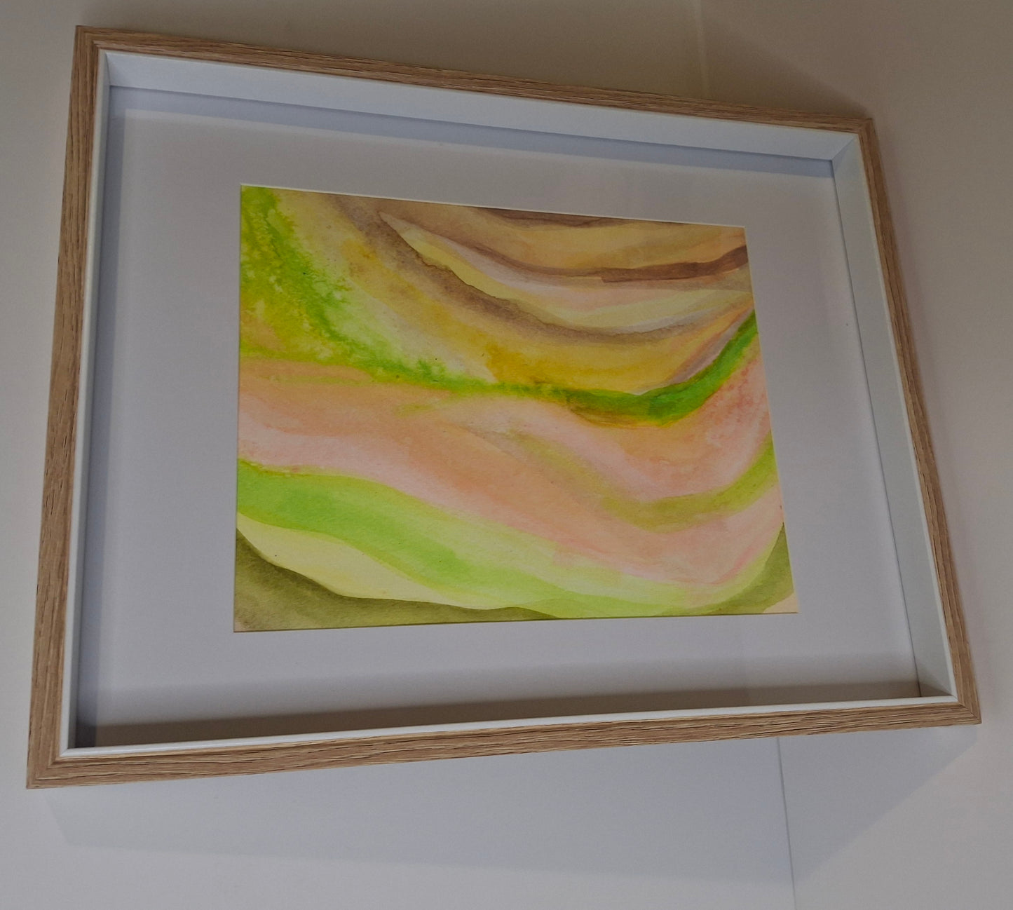 Framed abstract painting with soft pastel colors on a white wall