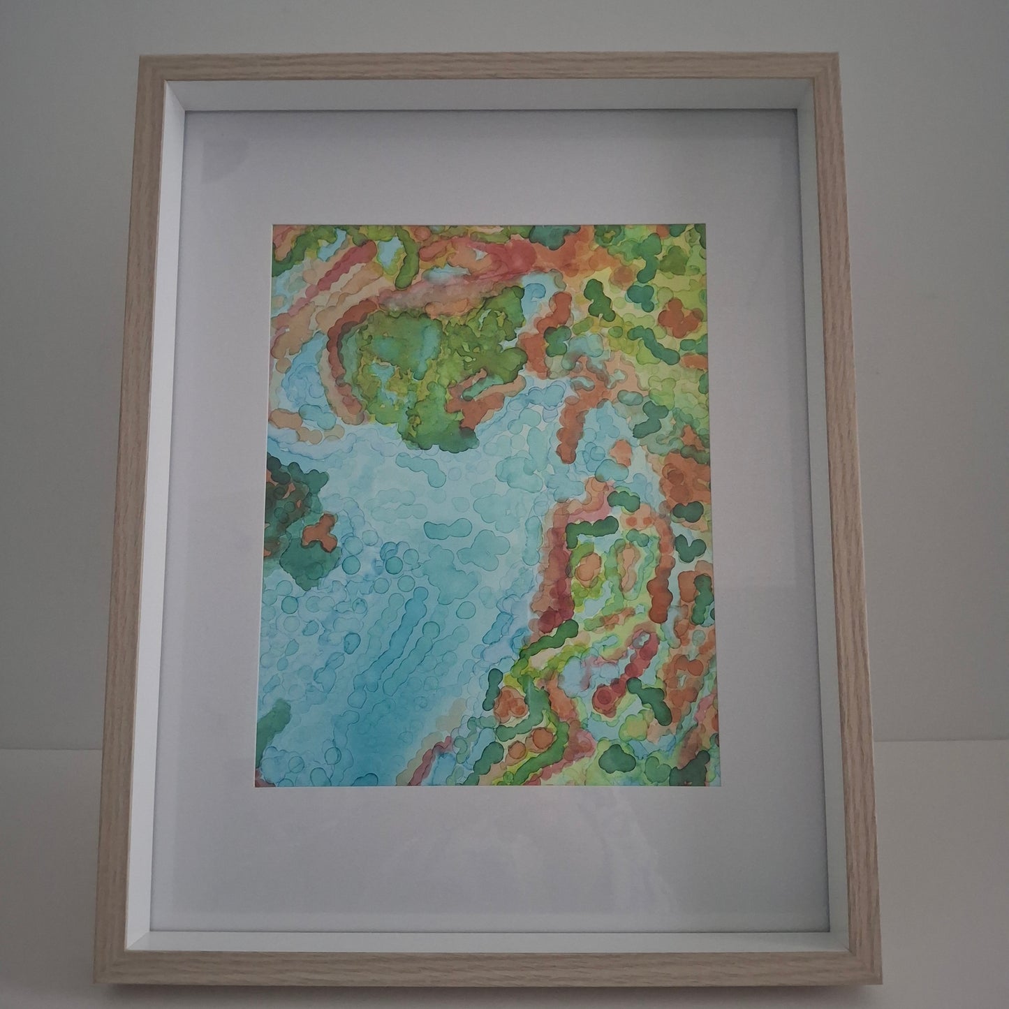 Framed abstract alcohol ink artwork titled Reef Dreaming by Elizabeth Marshall, featuring turquoise blue water forms with coral reef inspired patterns in green, orange, and red tones.