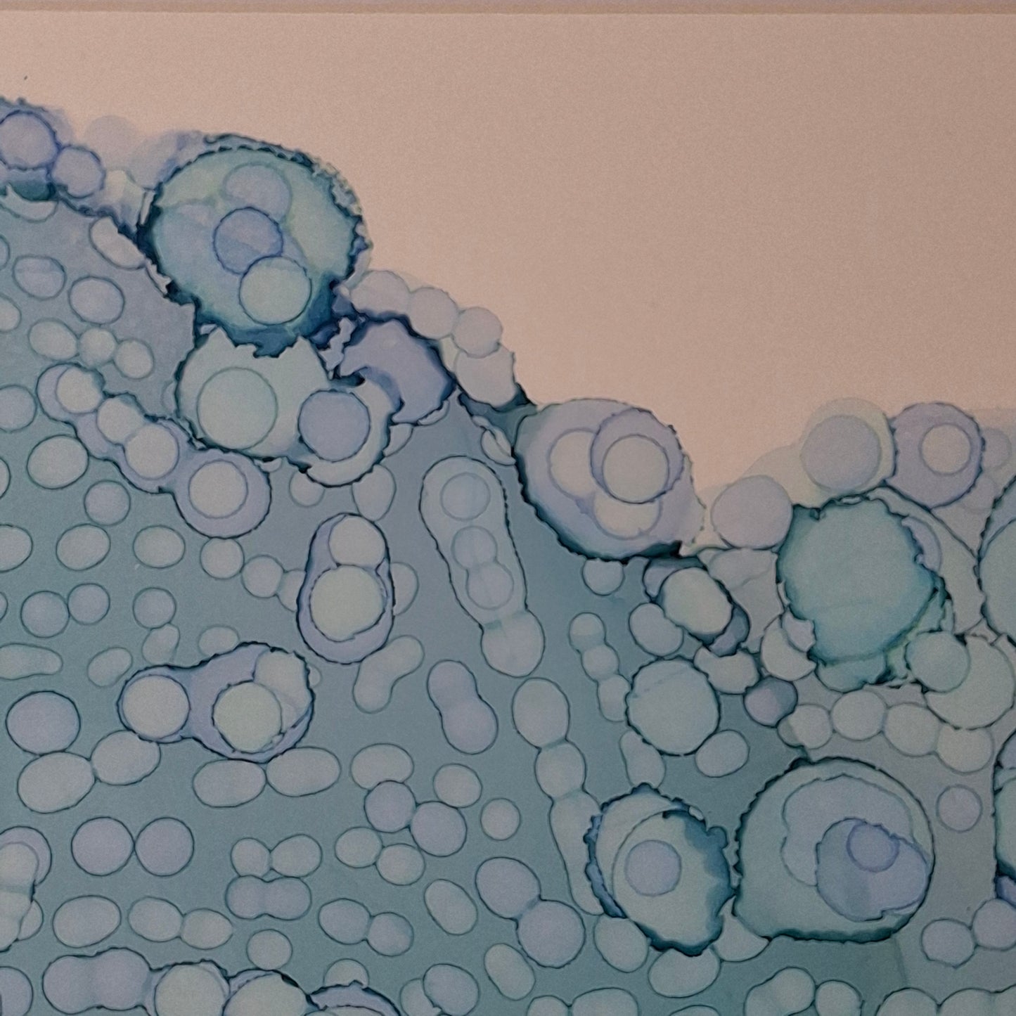 Framed blue alcohol ink artwork with overlapping bubbles and oceanic textures titled The Sea's Soft Embrace displayed in a coastal white kitchen