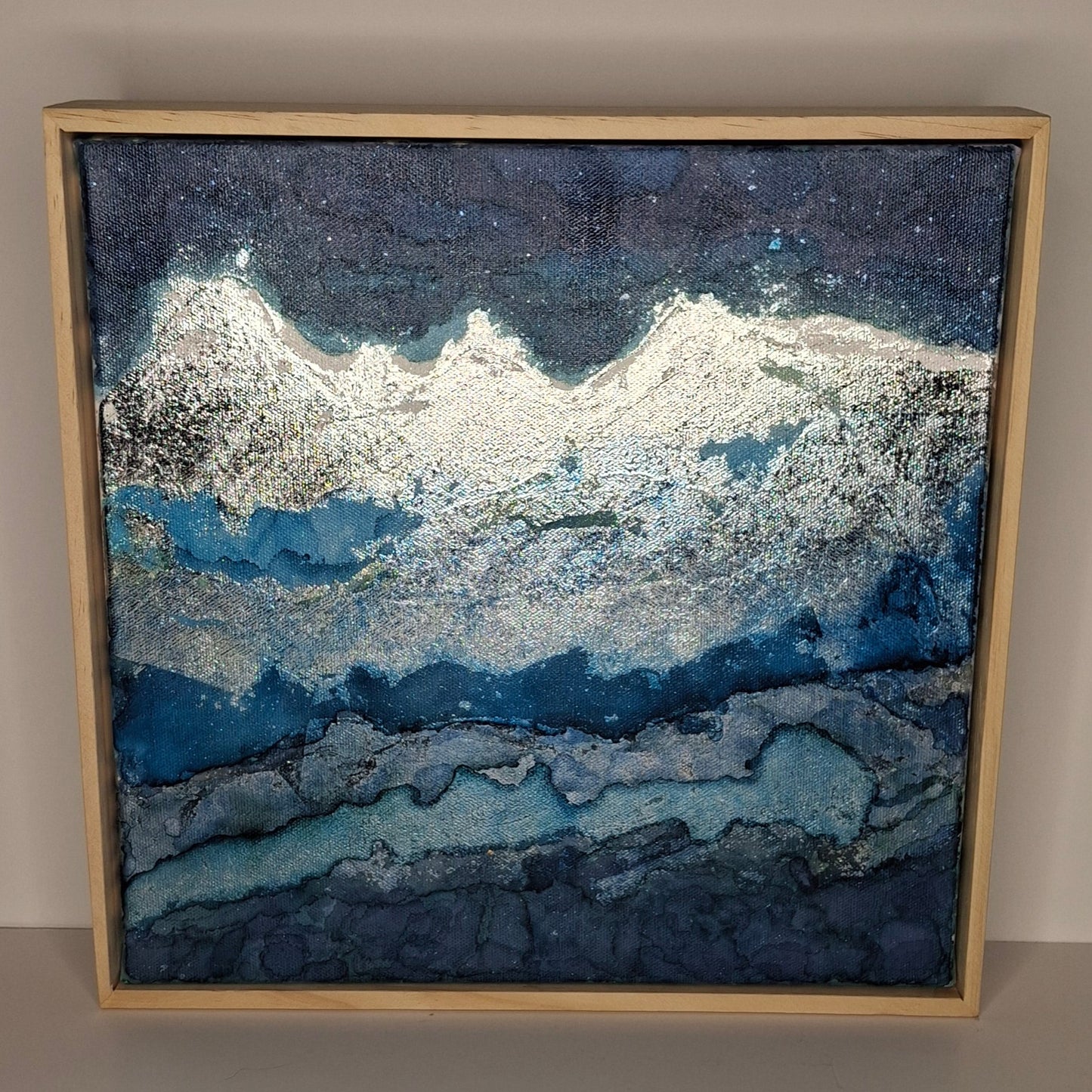 Framed abstract artwork with blue and silver patterns on a beige wall