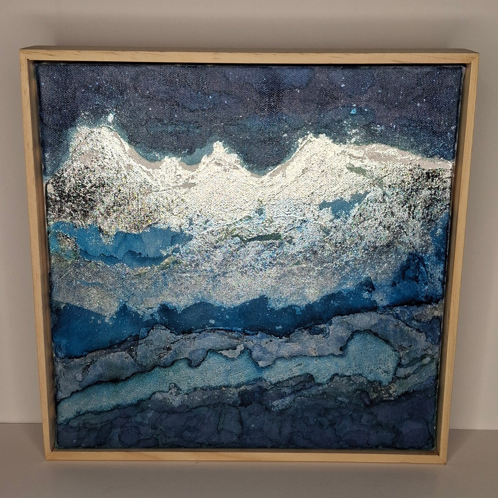 Framed abstract artwork with blue and silver patterns on a beige wall