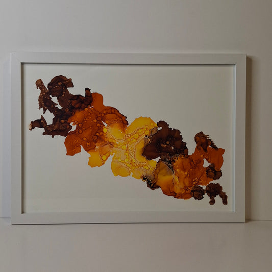 Framed abstract alcohol ink artwork titled Amber Drift hanging in a modern coastal-inspired room. The painting features warm amber and deep brown tones with organic flowing textures, displayed in a white frame