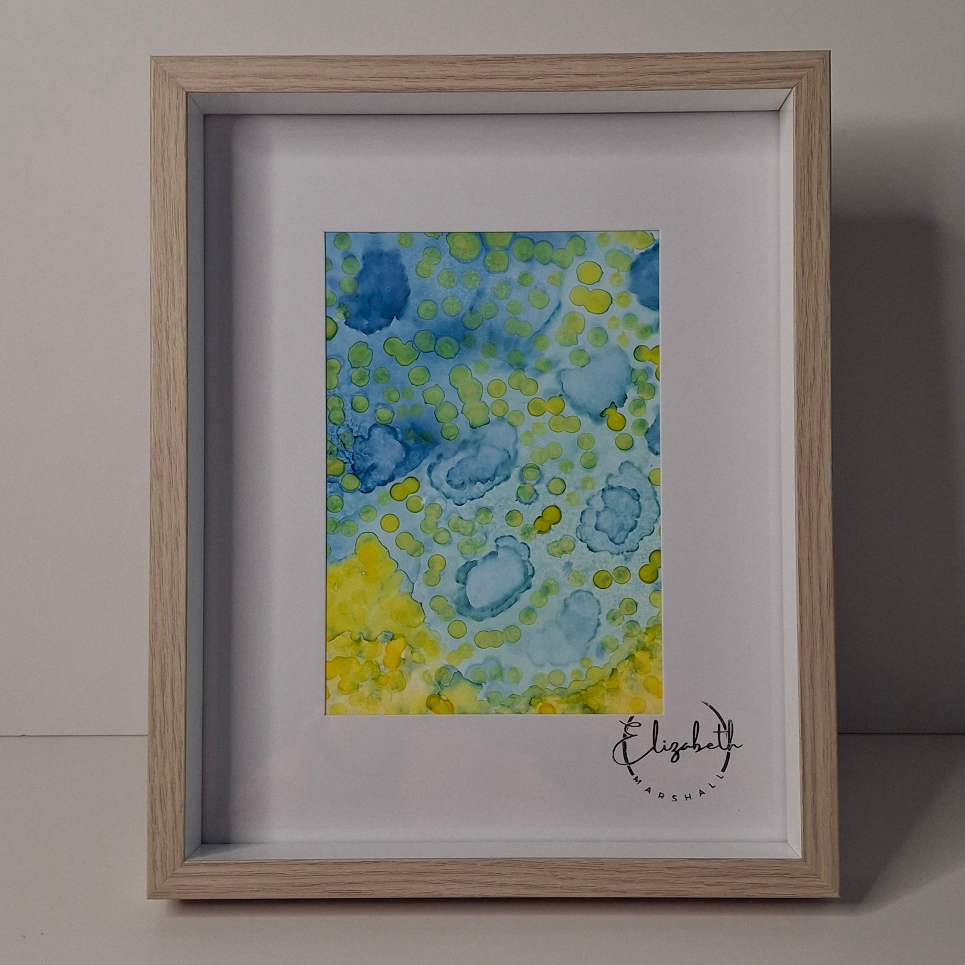 Framed painting with blue and yellow abstract design on a gray wall.
