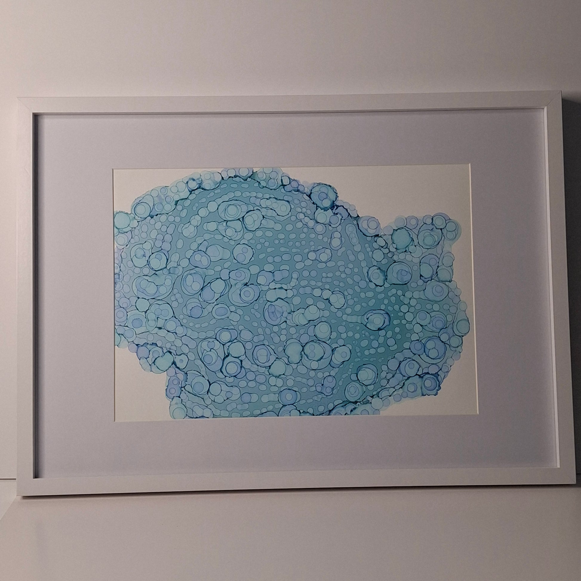 Framed blue alcohol ink artwork with overlapping bubbles and oceanic textures titled The Sea's Soft Embrace displayed in a coastal white kitchen